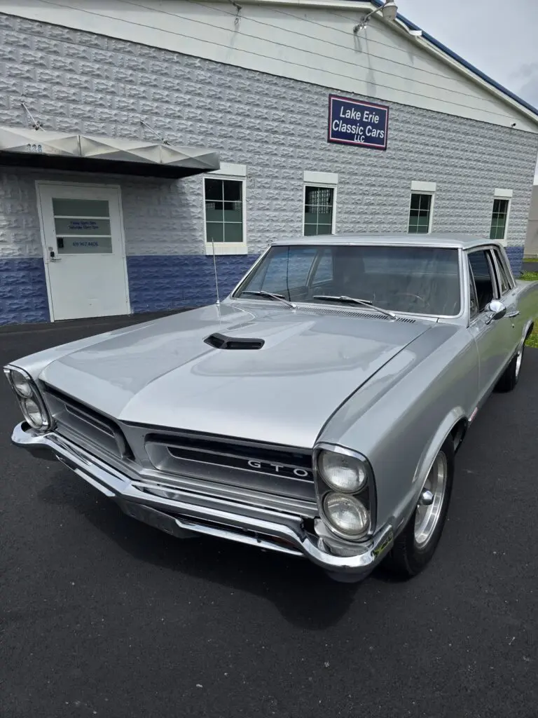Silver vintage GTO car outside classic car dealership.